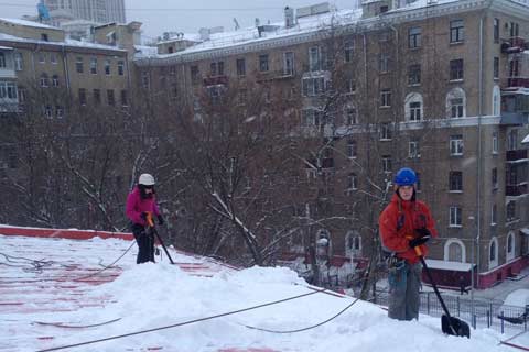 Альпинисты на страховке очищают плоскую кровлю от снега лопатами