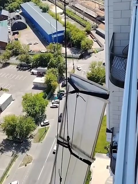 Стекло 3000×800 мм в обвязке поднимают вдоль фасада высотки
